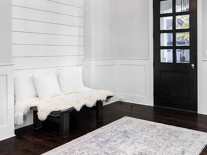 Small entry way with white walls and black door with a black wooden bench that has white pillow décor and fur blanket.